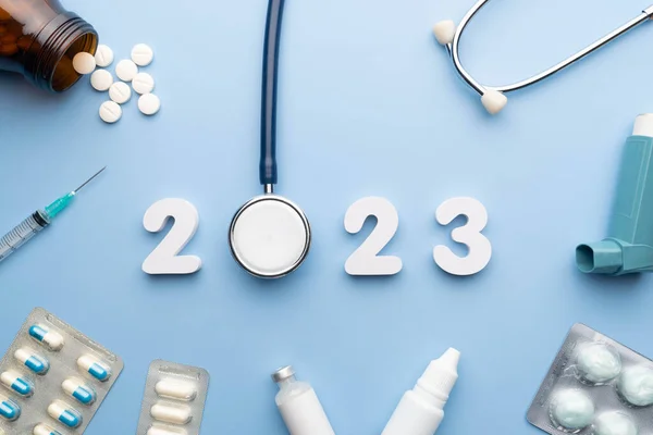 2023 Happy New Year banner for health care and medical concept. Stethoscope with doctor order chart, prescription, pills, syringe, vaccine vial and white number 2023 on table blue background.