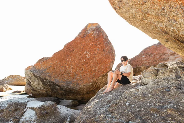 Wilson 's Promontory South Gippsland Avustralya' daki Squeaky plajında kayaların üzerinde oturan güneş gözlüğü takan bir çocuk.