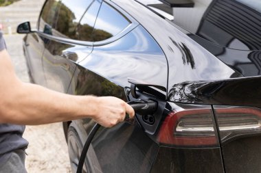 Elektrikli ev aracını şarj istasyonuna bağlayan bir adam.