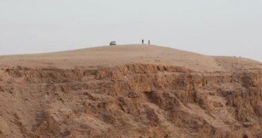 Two men shake hands at the top of a cliff in a desert landscape.