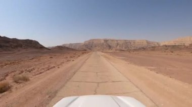 Dağlar ve mavi gökyüzüyle çölde bir kır yolunda giden araba..