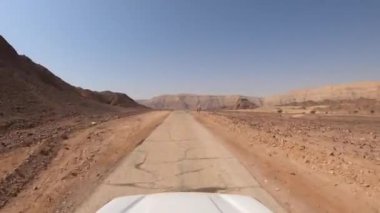 Dağlar ve mavi gökyüzüyle çölde bir kır yolunda giden araba..