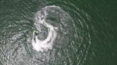 Hızlı su üzerindeki tepeden aşağı manzara. Jet ski daireler çiziyor ve açık yeşil Pasifik okyanus sularında güzel köpüklü dalgalar oluşturuyor..