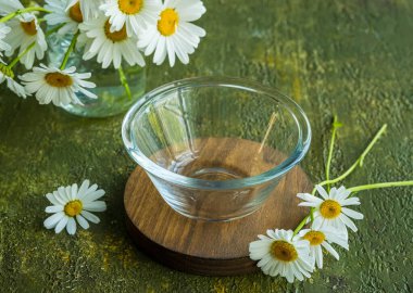 Ahşap tezgahta boş cam kase ve yeşil beton arka planda bir kavanozda papatya çayı. Yaz konsepti