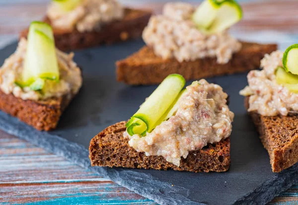 Appetizer, herring, onion and boiled egg forshmak on fried rye bread on a slate or stone board on a wooden background. Jewish cuisine. Fish recipes