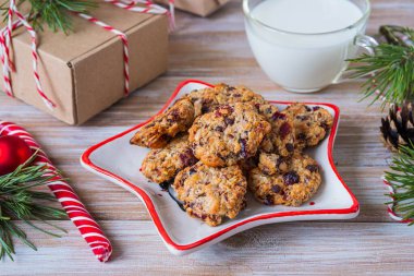 Yıldız şeklinde bir tabakta çikolata ve kızılcıklı yulaf ezmeli kurabiye ve tahta arka planda Noel Baba için şeffaf bir bardakta süt. Mutlu Noeller.