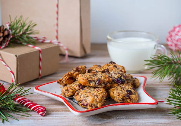 Yıldız şeklinde bir tabakta çikolata ve kızılcıklı yulaf ezmeli kurabiye ve tahta arka planda Noel Baba için şeffaf bir bardakta süt. Mutlu Noeller.