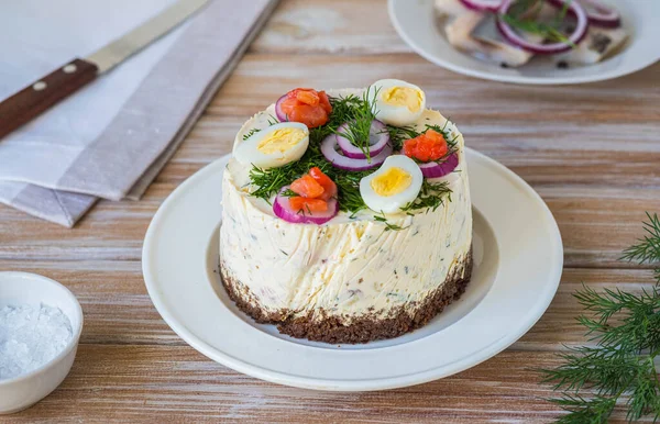 Snack, round Swedish salad cake with herring, potatoes, egg and sour cream mousse on black bread on a light plate on a wooden background. Christmas and Easter recipes. Swedish cuisine.
