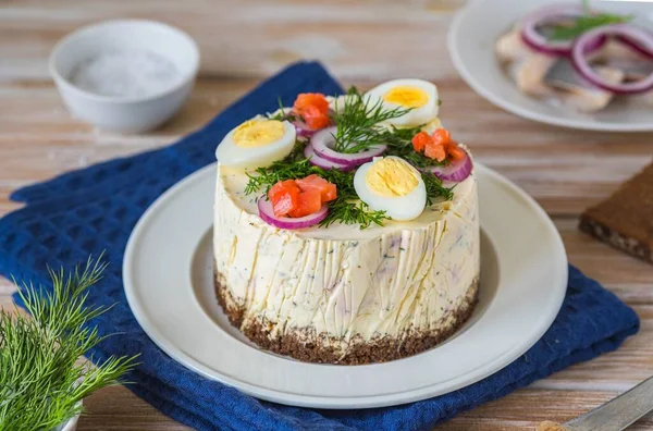 Snack, round Swedish salad cake with herring, potatoes, egg and sour cream mousse on black bread on a light plate on a wooden background. Christmas and Easter recipes. Swedish cuisine.