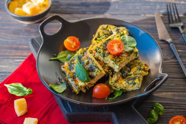 Sliced omelet or frittata with spinach and cheese on a black plate on a dark wooden background. Spinach recipes. Italian food.