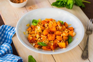 Haşlanmış beyaz pirinç, kızarmış kabak küpleri, soğan ve baharatlar ahşap tepside yuvarlak gri bir tabakta. Balkabağı tarifleri. Vejetaryen yemeği