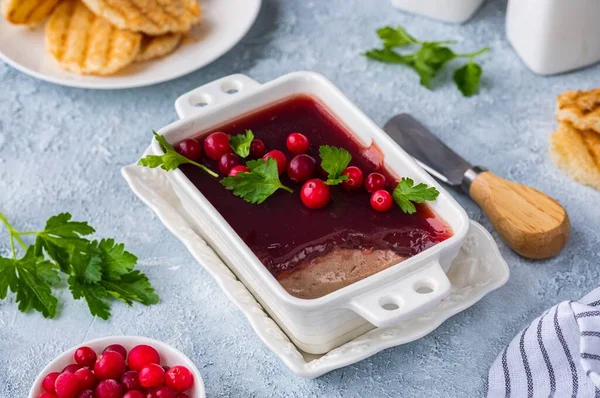 Cold appetizer, tender chicken liver pate with cranberry jelly garnished with cranberries and parsley in a white dish on a light concrete background. Liver recipes. French cuisine.