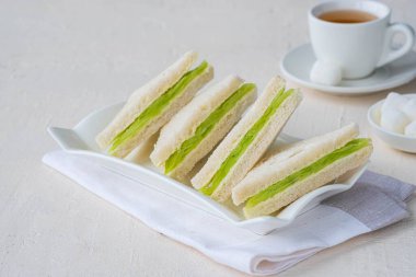 Tereyağlı üç köşeli çay sandviçleri ve açık beton arka planda beyaz bir tabakta taze salatalık dilimleri. Sandviç tarifleri. 