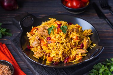 Pilaf, bir tabak pilav, tavuk, baharatlı havuç ve siyah bir ahşap zemin üzerinde kurutulmuş yaban mersini. Doğu mutfağı.