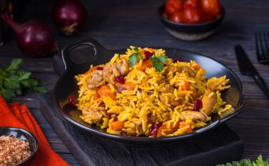 Pilaf, bir tabak pilav, tavuk, baharatlı havuç ve siyah bir ahşap zemin üzerinde kurutulmuş yaban mersini. Doğu mutfağı.