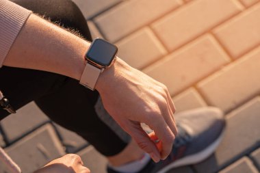 Formda bir kadın akıllı saati, giyilebilir teknolojiyi kontrol ediyor. Spor ayakkabısı spor koşusu, dışarıda yürüyüş. Sokakta koşu ayakkabıları ile yukarıdan görünüm.
