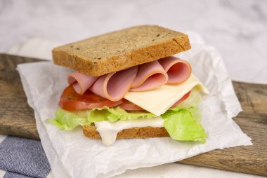 Jambonlu, domatesli, marullu ve peynirli klasik sandviç. Mutfak masasındaki dilimlenmiş kulüp sandviçi için tam tahıllı ekmek..