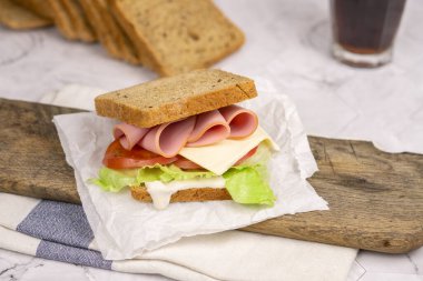 Jambonlu, domatesli, marullu ve peynirli klasik sandviç. Mutfak masasındaki dilimlenmiş kulüp sandviçi için tam tahıllı ekmek..