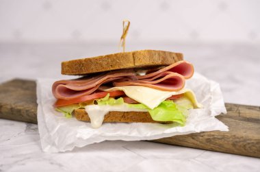 Jambonlu, domatesli, marullu ve peynirli klasik sandviç. Mutfak masasındaki dilimlenmiş kulüp sandviçi için tam tahıllı ekmek..