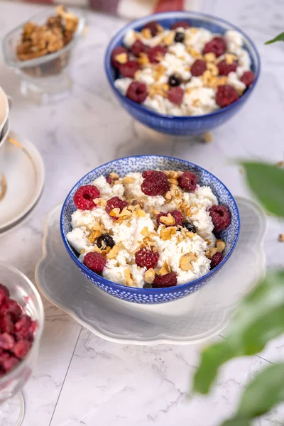 Blue bowl of cottage cheese with berries, honey and nuts for breakfast, selective focus.