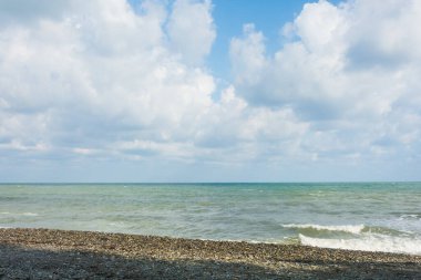 Çakıl taşlı deniz kıyısı ve beyaz bulutlu mavi gökyüzü.