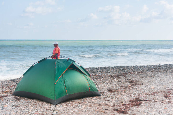 Зеленая туристическая палатка на пляже с галькой. Путешественник рядом с кемпингом.
