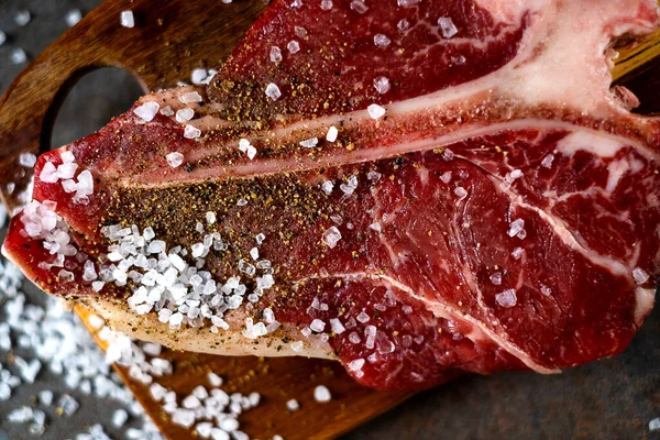 Raw T-bone steak cooking on stone table — Stock Photo, Image