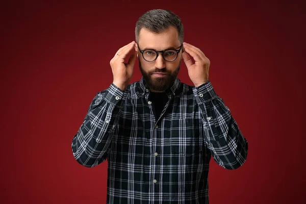 Ritratto di un uomo fresco con la barba, che tiene gli occhiali con due mani Fotografia Stock