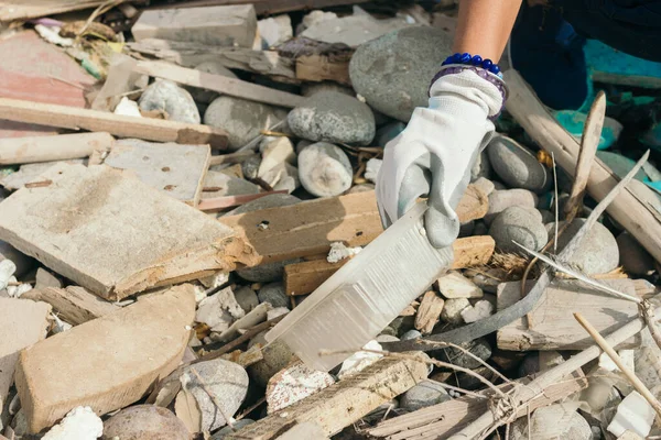 Elinde plastik bir çarşaf olan bir kadının eli sahildeki taşlarda daha fazla çöp topluyor. Boşluğu kopyala