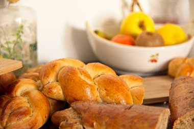 Ziyafet, dağınık masa. Saç örgüsü şeklinde bir ekmek. Tatlı Challah. Kahvaltı, yan görüş. Kiraz domatesleri ve zeytinyağı, Balzamik sirke, Atlantik tuzu ve meyveler 
