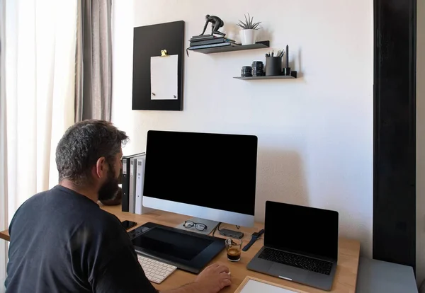 A Caucasian man sits at a desk at the home office looking at a computer screen. The great resignation concept. A male works on a computer online workplace. Mockup Copy Space. Hebrew English keyboard — стокове фото