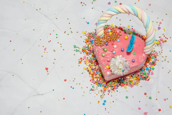 Pink heart shape cake on a white marble background with a lot of small colorful candies . Valentine day. About love. copy space — Stock Photo, Image