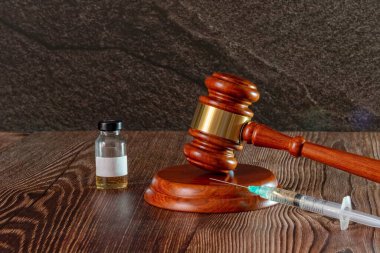 Hakimler çekiç, şırınga ve aşı şişesini ahşap arka planda tutuyor. Tıbbi yargılama kavramı