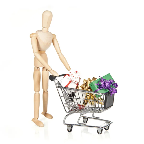 Wooden character with shopping cart and Christmas gifts — Stock Photo, Image