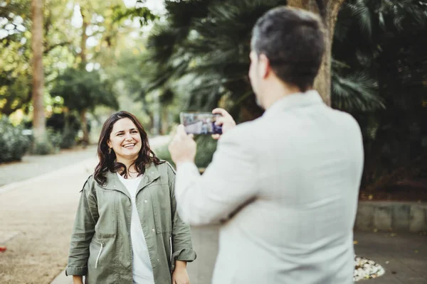 Parkta cep telefonu olan bir kadının fotoğraflarını çeken bir adam.