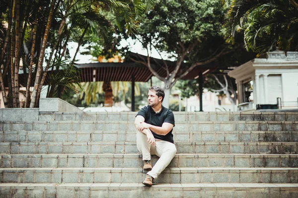 Şehir parkında merdivenlerde oturan bir adam bekliyor.