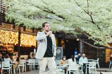 Parkta kahve içip sağa bakan dalgın bir iş adamının yatay görüntüsü.