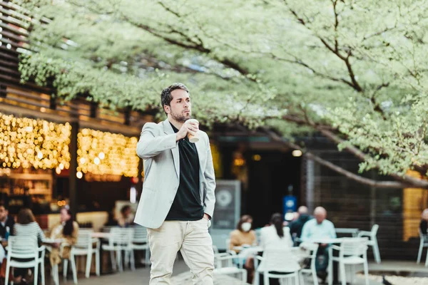 Parkta kahve içip sağa bakan dalgın bir iş adamının yatay görüntüsü.