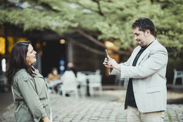 Bir adam, kafenin yanındaki parkta bir kadının cep telefonuyla fotoğraf çekiyor.