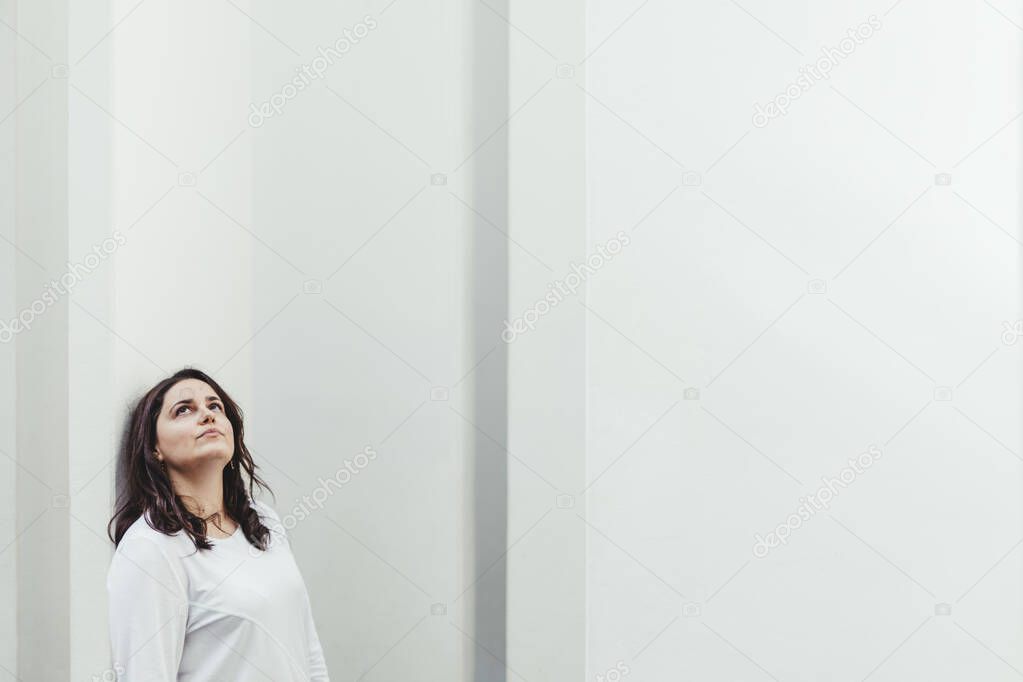 Medium shot of serious woman leaning against white wall with white columns background