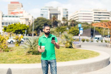Adam elinde kahveyle cep telefonuna bakıyor.
