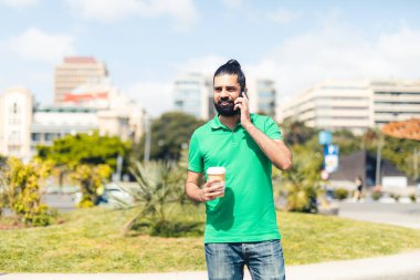 Şehirde elinde kahveyle cep telefonuyla konuşan bir adam.