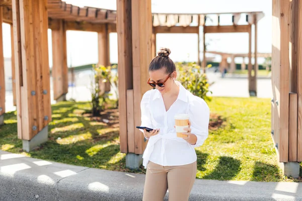 Elinde kahveyle cep telefonuna bakan bir kadın.