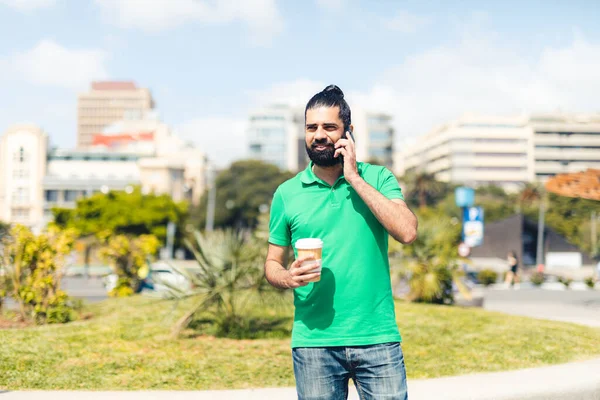Şehirde elinde kahveyle cep telefonuyla konuşan bir adam.