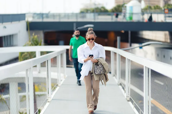 Gülümseyen kadın ve erkek cep telefonuna bakarak şehir yolunda yürüyorlar.