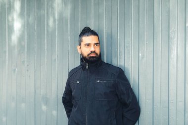 Yatay çizgileri olan metal bir arka plana yaslanan ciddi bir adam.