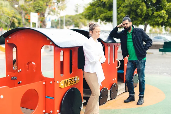 Parkta oyuncağa yaslanan bir kadına ve onu izleyen bir adama odaklan..