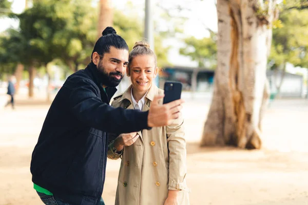 Kadın ve erkek şehir parkında selfie çekiyorlar.
