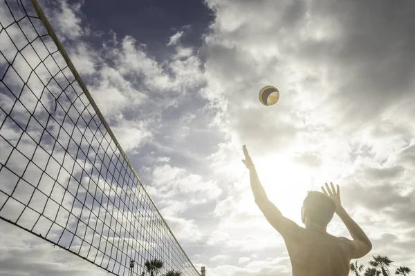Adamın biri plaj voleybolunu ışığa doğru fırlatıyor. Yaz tatili kavramı