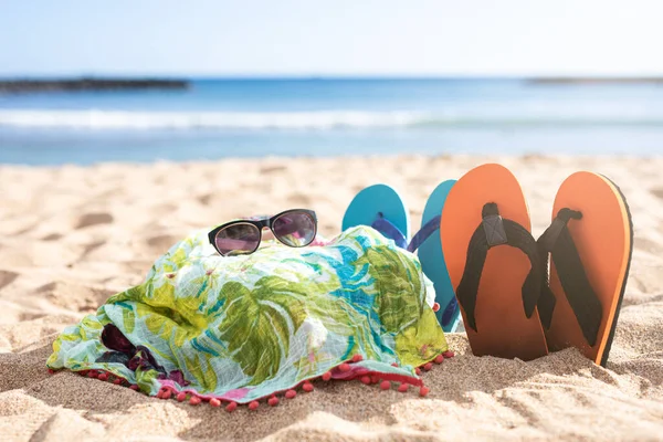 Pareo, güneş gözlüğü ve terlikler güneşli bir kumsalın kumlarında